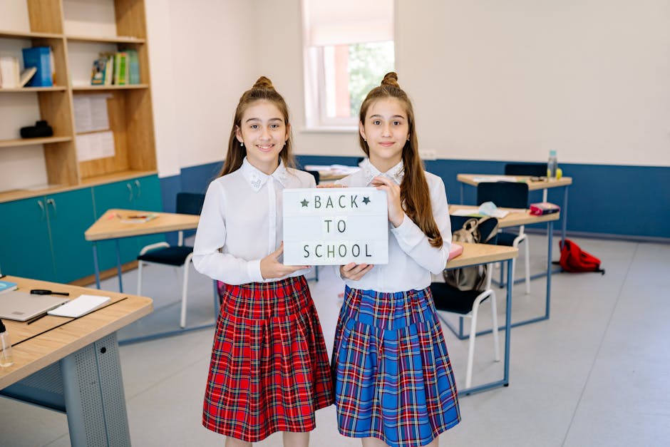 Twin sisters in uniforms holding a back to school sign, standing in a classroom.